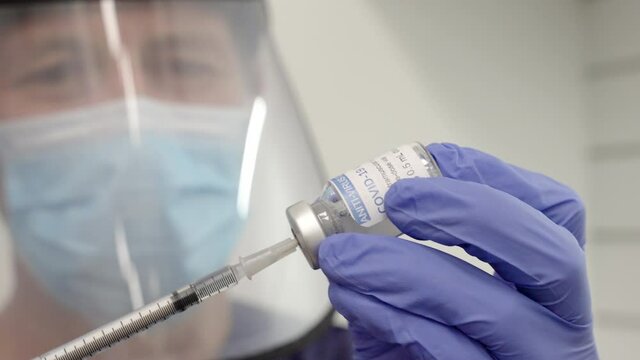 close uo of a male healthcare worker in ppe fills a syringe from a covid-19 vaccine