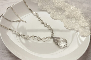 Plakat Detailed shot of beautiful luxury necklace chain with a large transparent crystal pendant on white ceramic plate