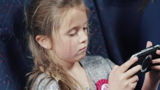 A family with mother and two daughters are sitting on an airplane airliner. The girls are entertained with games and books. The passenger plane has blue seats and tray tables.