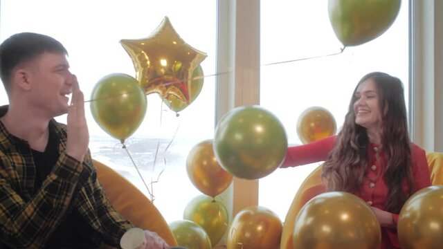 Happy couple sits in a restaurant in front of a window with beautiful view of the snow-capped mountains and plays with balloons. A guy throws a balloon at a girl. A fun first date on Valentine's Day.