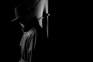 dark silhouette of a man in a raincoat with a hat at night