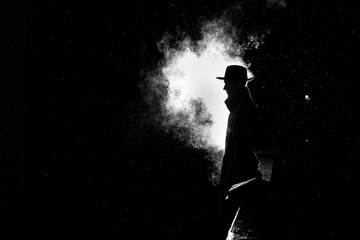 dramatic silhouette of a dangerous man in a hat at night in the rain in the city - obrazy, fototapety, plakaty