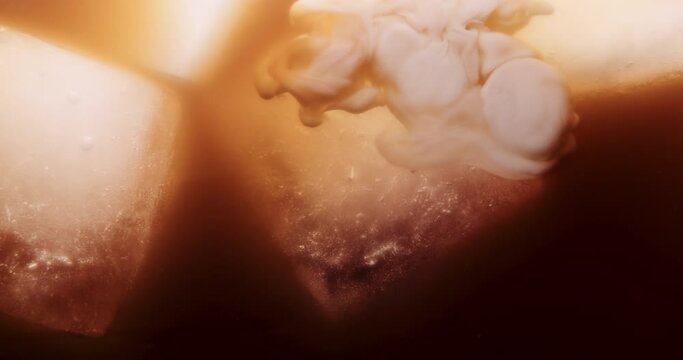 Cream or milk poured into an iced coffee, tea, frappe, Frappuccino on ice cubes