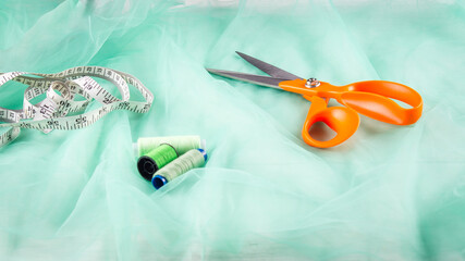 Scissors tailor and inch, centimeter tape and green threads on a background of  green tulle fabric. Tailor's equipment. Sewing tools.