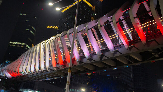 a pedestrian bridge covered in colorful neon lights at night in the Senayan City Jakarta area