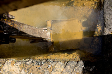 Rusty excavator shovel under dirty water at a hole from the sewerage system in the street