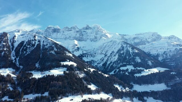 Amazing drone flight of a stunning alpine valley, village and snow covered mountain peaks in Champery, Switzerland. A beautiful winter wonderland scenic flight on a clear blue sky day.