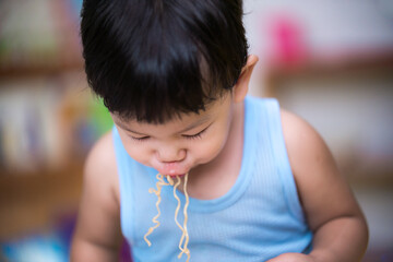 Handsome little children are sucking instant  noodles into the mouth.  Asian child wears a blue tank top.  Little kid between 1 - 2 years old