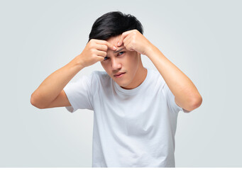 A handsome young Asian man squeezes a pimple on his forehead.
