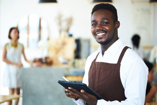 A black male waiter is standing and friendly smiling.