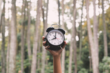 Classic alarm clock in a hand with trees blurry on the background. Clock that symbolizes the time...