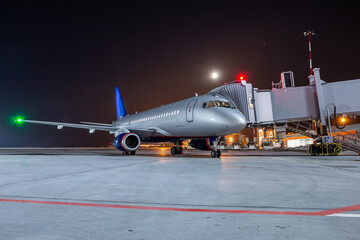 Modern passenger airliner at the jet bridge on night airport apron