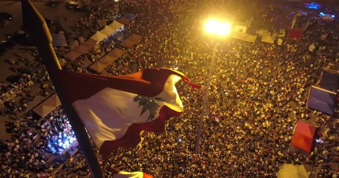 Beirut, Lebanon 2019 : night drone turn around shot on Lebanese flag in Martyrs' Square while hundreds of protesters are revolting against government failure during the Lebanese revolution