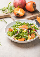 Delicious persimmon salad with arugula  and orange served on light grey table, flat lay. Space for text
