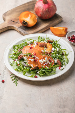 Persimmon salad with arugula, nuts, goat cheese, pomegranate. Healthy vegetarian food concept.