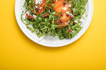 Persimmon salad with arugula, nuts, goat cheese, pomegranate. Healthy vegetarian food salad concept.