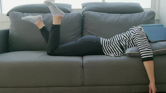 Young Asian girl sleeping on sofa feeling tired bored lazy sleeping book covering face, tired late night study prepare for exam, in living room quarantine education teenage procrastination lifestyle