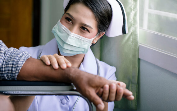 Young Nurse Woman Wearing Face Mask Taking Care Of Elderly Man Patient Sitting On Wheelchair In The Hospital, Close Up