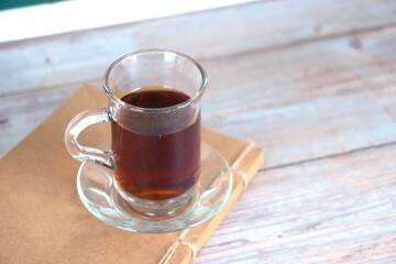There is a book and a cup of black tea on the table