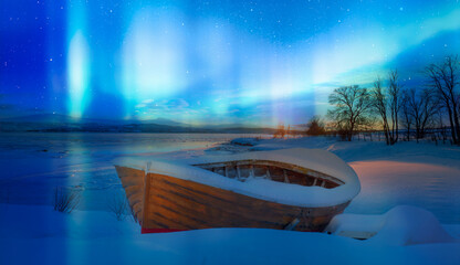 Red wooden boat covered with layers of snow - Aurora Borealis in Tromso, Norway in front of the Norwegian fjord 