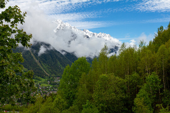 View of the French Alps near the summit of Mont Blanc at the entrance of the Mont Blanc Tunnel between France and Italy. There is a thick forest, snowy mountain tops, cottages on the foothills.