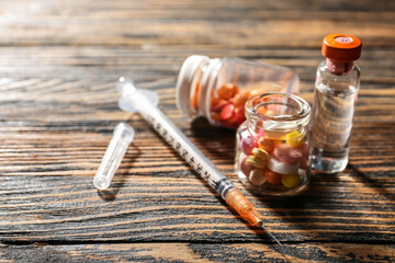 Syringe and bottles with pills on wooden background