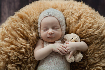 Cute newborn baby sleeping on brown fur blanket with stuffed teddy bear toy. Baby goods packaging template. Healthy and medical concept. Copy space