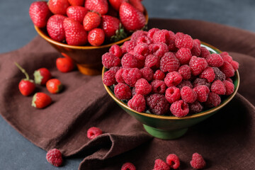 Bowls with ripe strawberry and raspberry on dark background