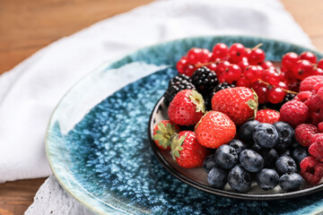 Plate with different tasty berries on wooden table