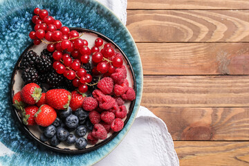 Plate with different tasty berries on wooden table