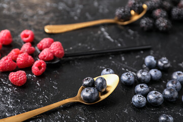 Spoons with different berries on dark background