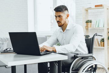 Serious concentrated man in wheelchair using his laptop for work / seeking a job in internet