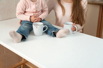 Big white cups in female and baby hands. Breakfast in family, details