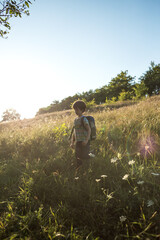 A boy with a backpack walks in the meadow