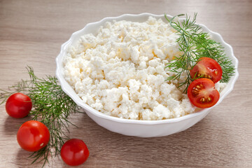 Rustic cottage cheese in white bowl with fresh vegetables on the kitchen table. Appetizer of tomatoes; peppers; cottage cheese; sour cream and spices.