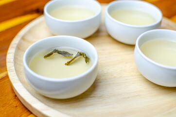 Tea set of white cups and pot pouring water on red wood table and brown wooden tray, Japanese and Chinese jasmine green tea. Tradition herbal brewing for relaxation.