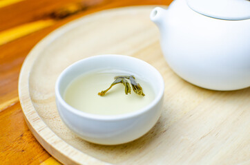 Tea set of white cups and pot pouring water on red wood table and brown wooden tray, Japanese and Chinese jasmine green tea. Tradition herbal brewing for relaxation.