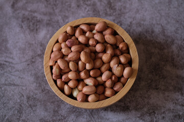 Raw Groundnuts in the wooden bowl on cement background. Top view. 