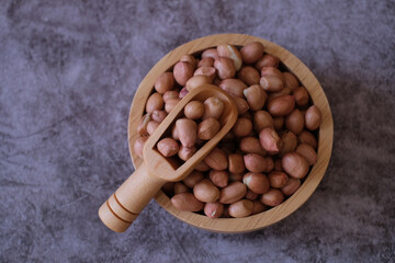 Raw Groundnuts in the wooden bowl and the wooden scoop on cement background. Top view. 
