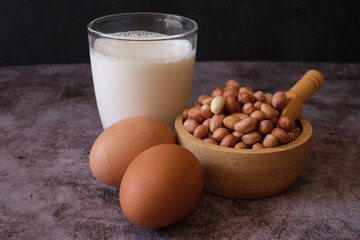 Protein food group. Raw Groundnuts in the wooden bowl, chicken egg and a glass of milk on cement background. healthy food.