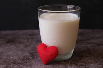 A glass of cold milk and a little heart shape with dark wall background. Concept of health care.