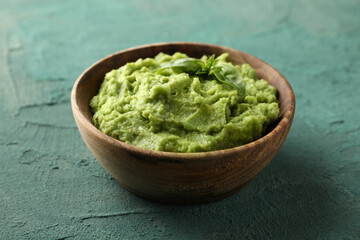 Bowl of guacamole on green textured background, close up