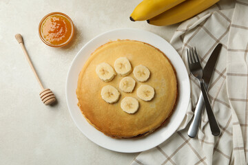 Concept of breakfast with plate of thin pancakes with banana, and jam on white textured background