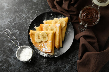 Concept of delicious breakfast with crepes with sugar powder and banana on black smokey background