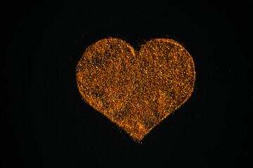 Heart made of golden sand from sequins. Sequins on a black background.