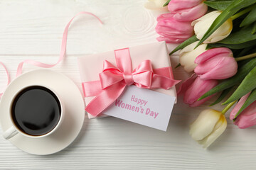 Text Happy Women's Day, tulips, gift box and cup of coffee on white wooden background, top view