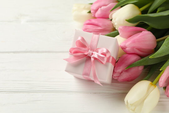 Beautiful tulips and gift box on white wooden background