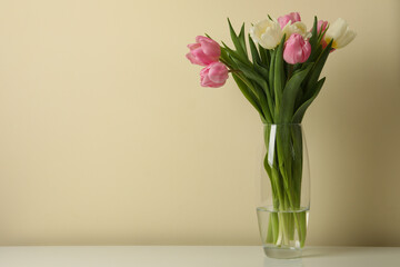 Vase with tulips against beige background, space for text
