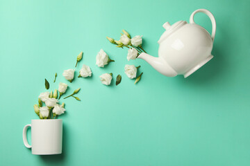 White roses pouring from a teapot into a cup on a mint background
