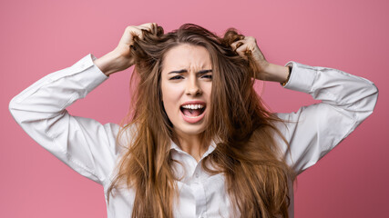 Portrait of woman in panic shouting and grabbing her head in fear or frustration. Studio shot, pink background